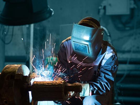 Un hombre que lleva una máscara de soldador está soldando una pieza de metal en una fábrica.