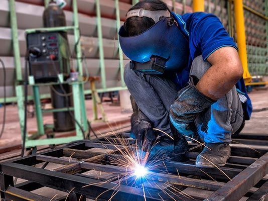 Un hombre está soldando una pieza de metal en una fábrica.