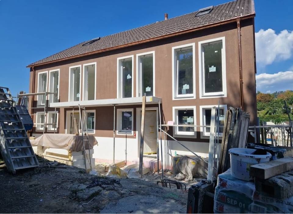 Moderne Küche mit dunklen Holzschränken, schwarzen Arbeitsplatten, weissen Fliesenböden und Fenstern an der rechten Wand