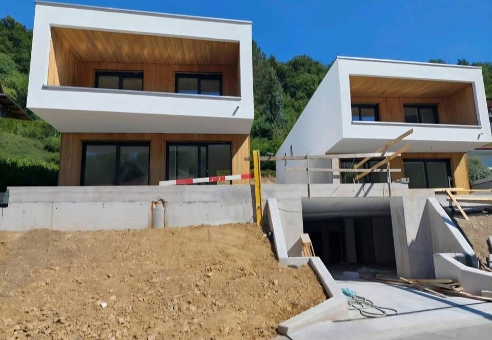 Zwei moderne, weisse Häuser im Bau an einem Hang, mit sichtbarem Holz im Inneren und unfertigem Gelände