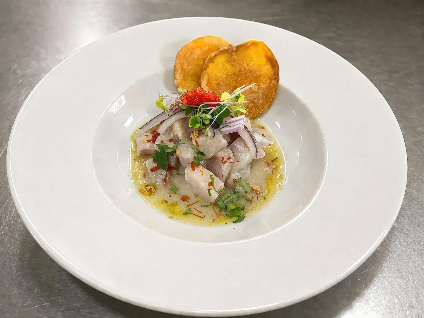 Ceviche en un tazón blanco adornado con hierbas, acompañado de dos chips de plátano dorados en un plato blanco.
