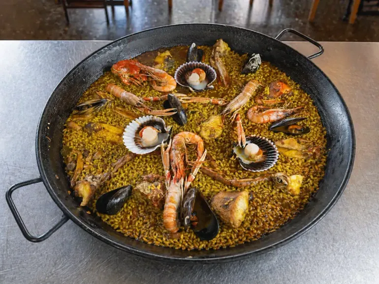 Langosta a la parrilla con salsa servida en un plato ovalado blanco.