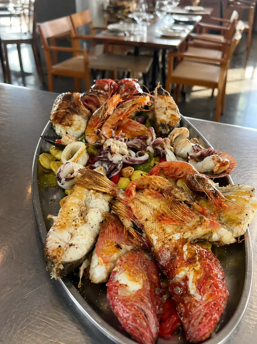 Dos paelleras grandes, una oscura y otra dorada, con una taza pequeña de salsa al lado.