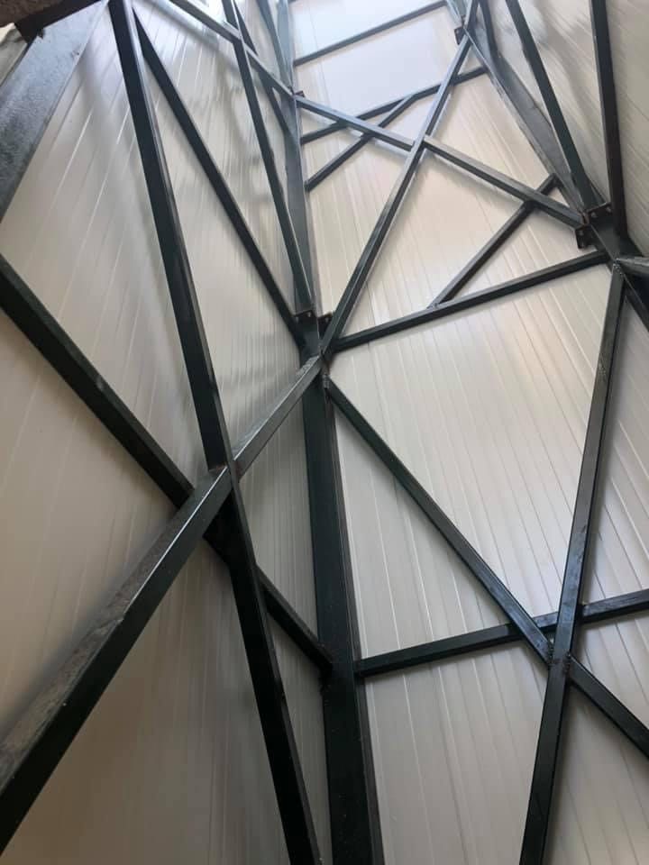 Χαλύβδινες δοκοί που διασχίζουν μια ανοιχτόχρωμη γκρι κυματοειδή οροφή, όπως φαίνεται από κάτω