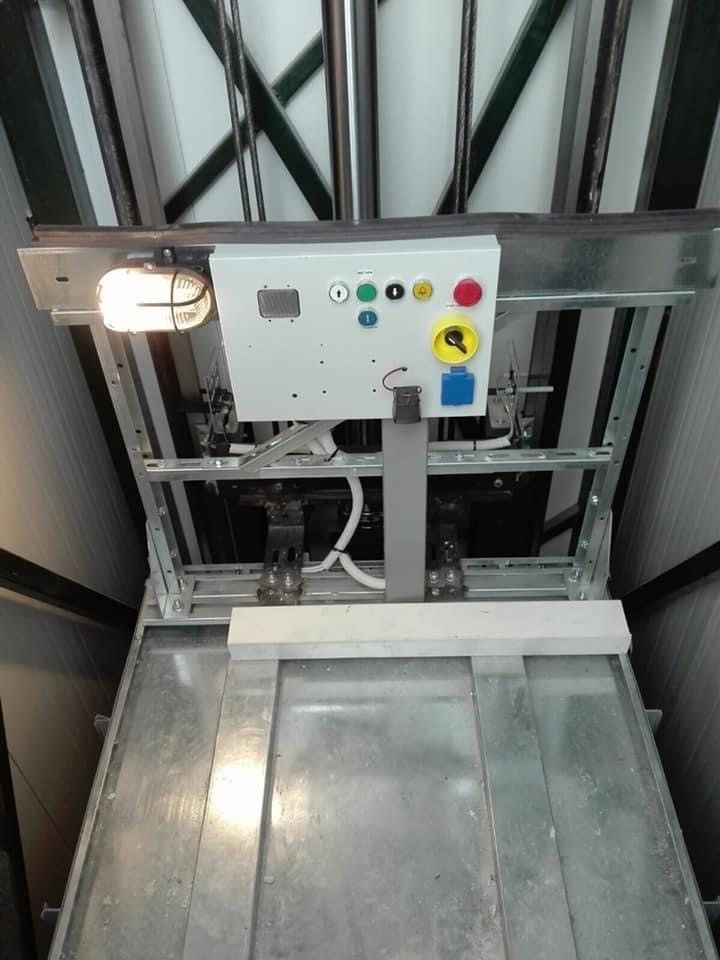 Βιομηχανική πλατφόρμα ανύψωσης με μεταλλική πύλη, πίνακα ελέγχου και προειδοποιητική λυχνία μέσα σε φρεάτιο μηχανημάτων.