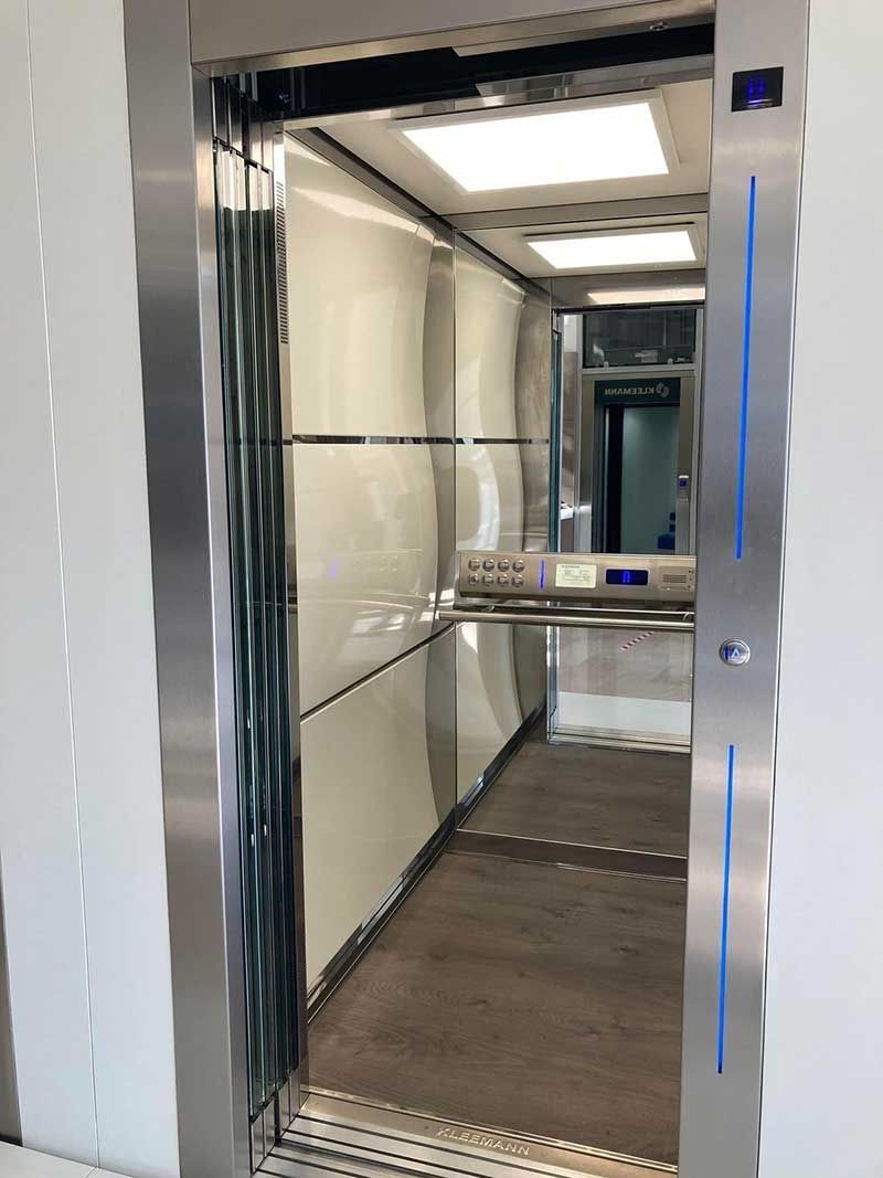 Εσωτερικό ανελκυστήρα από ανοξείδωτο ατσάλι με ανακλαστικούς τοίχους, φωτεινά φώτα οροφής και ανοιχτή πόρτα.