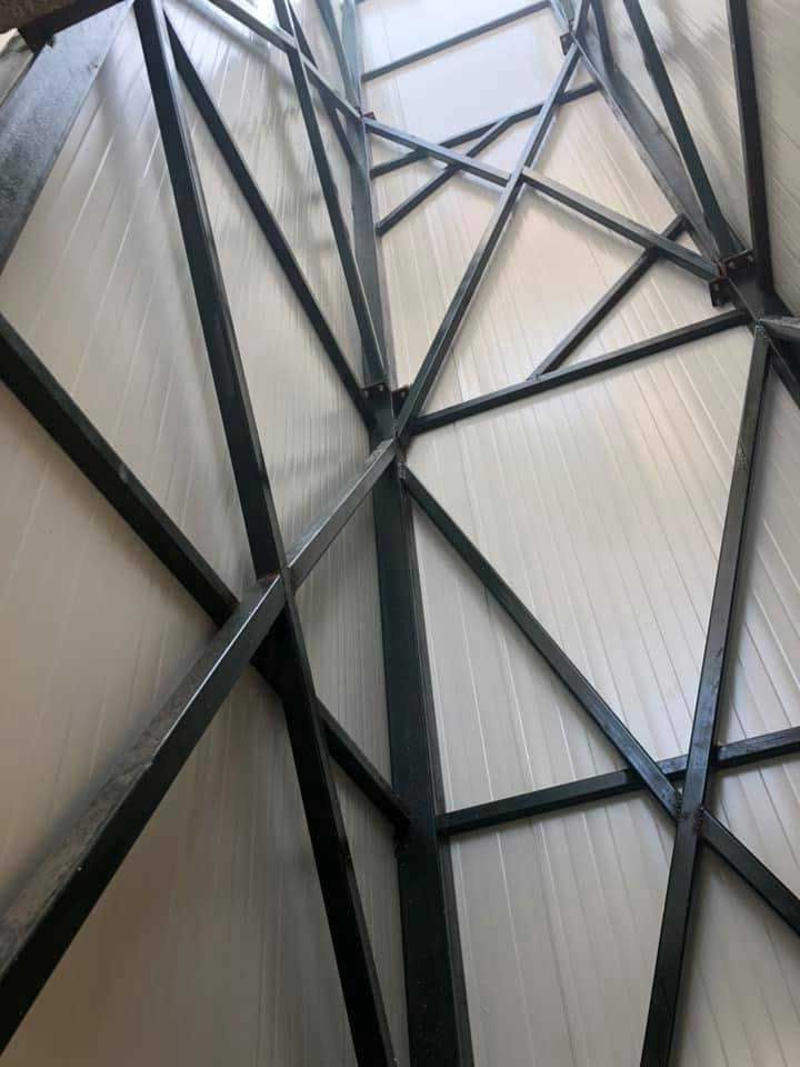 Γεωμετρικές χαλύβδινες δοκοί που διασχίζουν μια ανοιχτόχρωμη οροφή, δημιουργώντας ένα αφηρημένο αρχιτεκτονικό μοτίβο