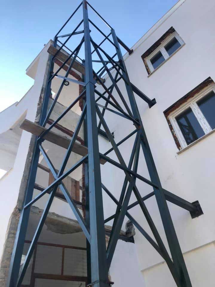 Ψηλός μπλε μεταλλικός πύργος δίπλα σε ένα λευκό κτίριο κάτω από έναν καθαρό ουρανό