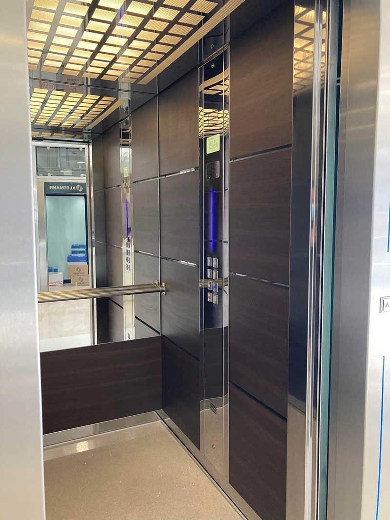 Σύγχρονο εσωτερικό ανελκυστήρα με γυαλιστερά σκούρα πάνελ, καθρέφτη τοίχο και μπεζ δάπεδο