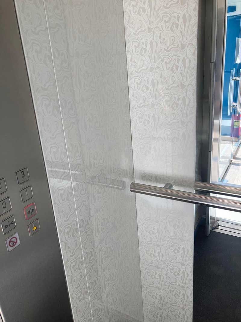 Μέσα σε έναν ανελκυστήρα, ένα μεταλλικό κιγκλίδωμα δίπλα σε γκρι τοίχους με υφή και ένας πίνακας ελέγχου.