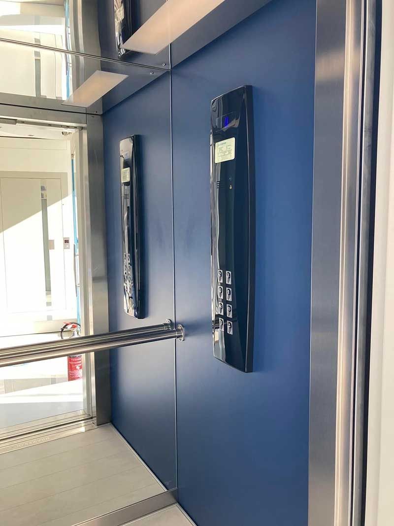 Μπλε τοίχος με δύο επιτοίχιες μαύρες ιατρικές συσκευές σε έναν φωτεινό διάδρομο