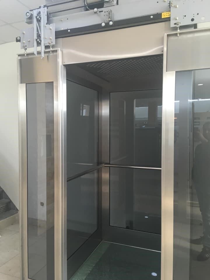 Σύγχρονος γυάλινος ανελκυστήρας με ανοιχτές πόρτες και πλαίσιο από ανοξείδωτο χάλυβα σε ένα λόμπι κτιρίου