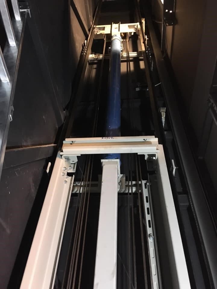 Εσωτερικό ενός ψηλού φρεατίου ανελκυστήρα με ράγες και μηχανήματα, φωτισμένο από ψηλά σε έναν στενό βιομηχανικό χώρο