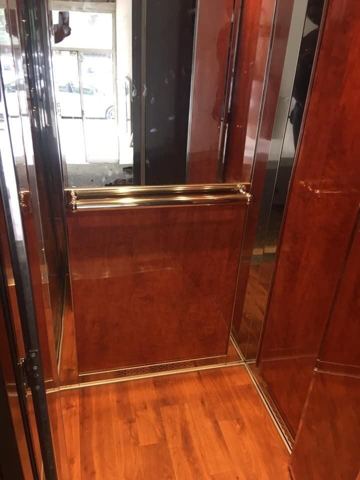 Εσωτερικό ανελκυστήρα με ξύλινη επένδυση, χαμηλωμένο μεταλλικό φράγμα και γυαλιστερό ξύλινο δάπεδο.