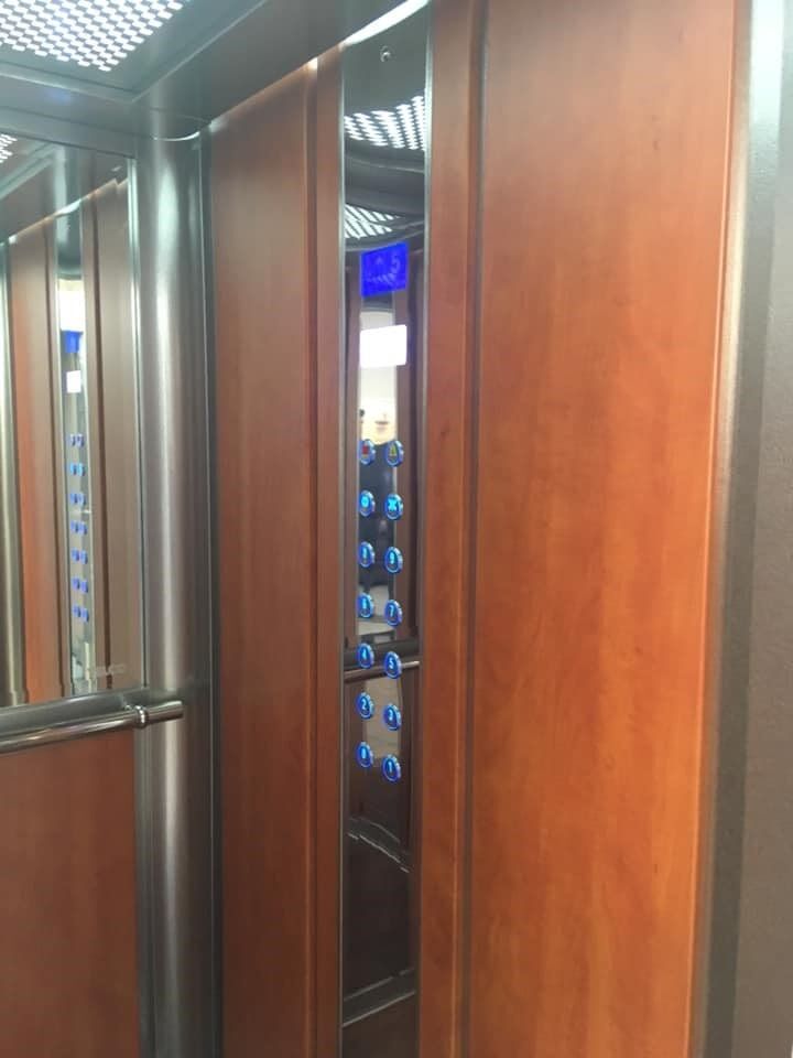 Μέσα σε έναν ανελκυστήρα, μια μερικώς ανοιχτή πόρτα αποκαλύπτει έναν διάδρομο με οθόνες με μπλε φωτισμό.