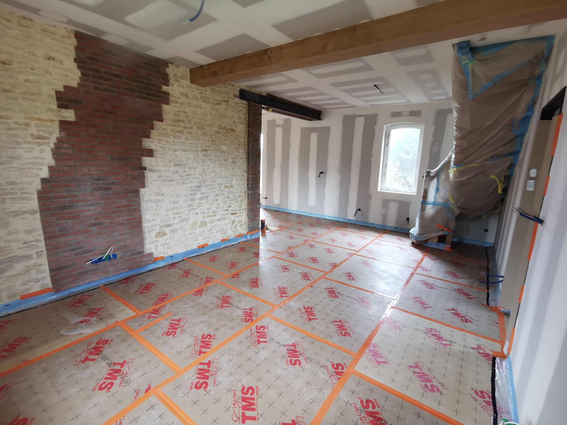 Intérieur d'une pièce en construction avec briques apparentes, poutres en bois et isolation du sol.