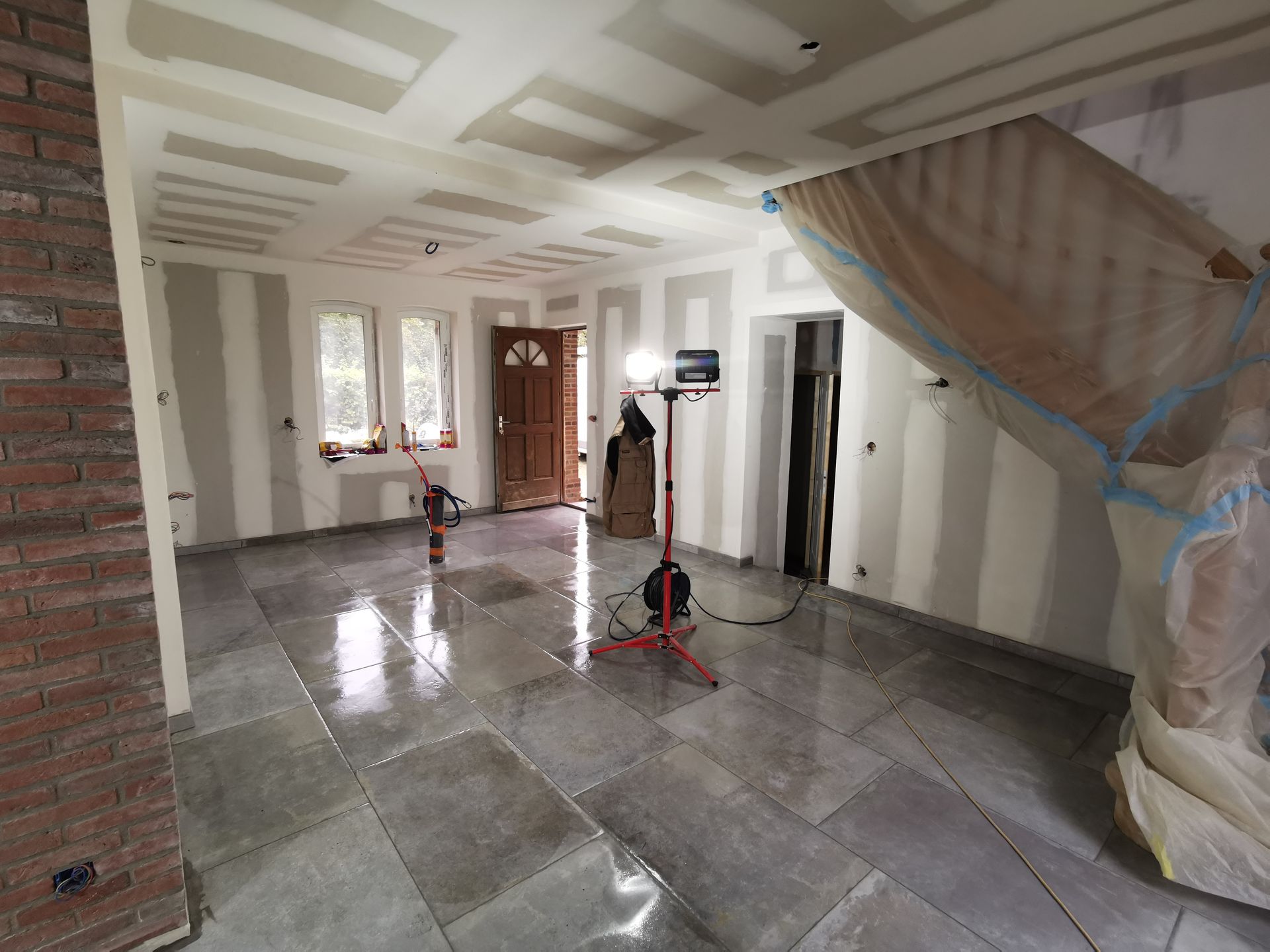 Rénovation intérieure : pièce inachevée avec nouveau carrelage au sol, cloisons sèches apparentes et éclairage de chantier.