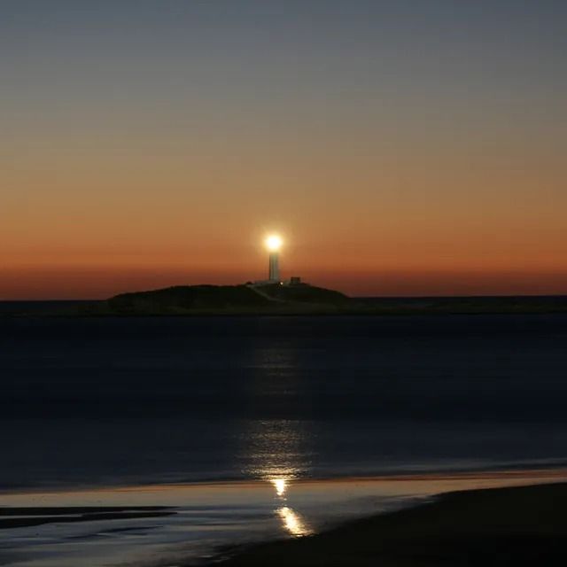 Un faro en una colina con vistas al océano al atardecer.