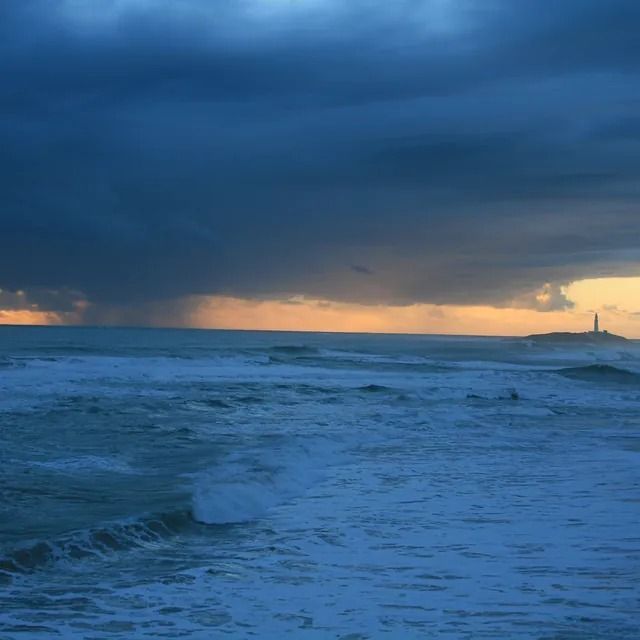 Hay un faro a lo lejos y un cielo tormentoso sobre el océano.