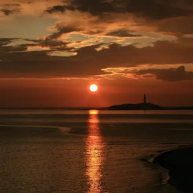 El sol se está poniendo sobre el océano con un faro en la distancia.