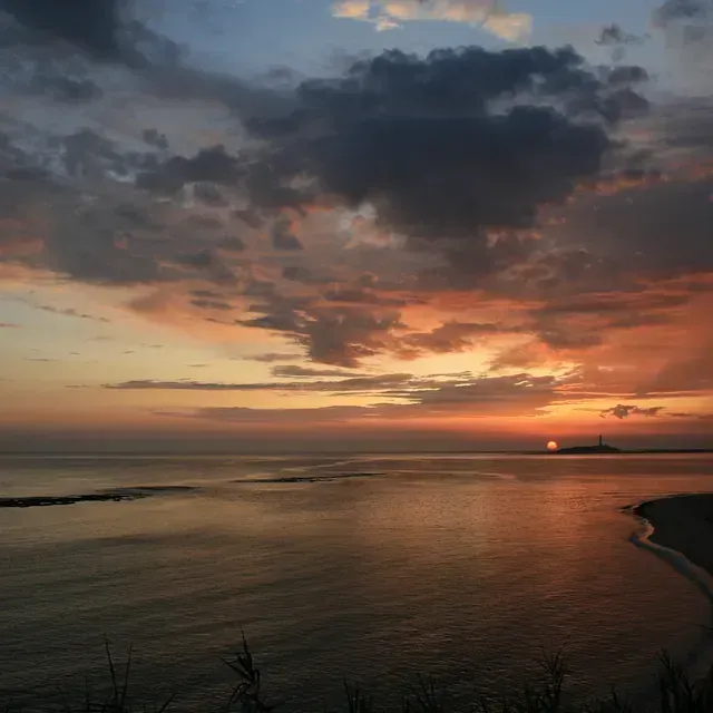 Una puesta de sol sobre un cuerpo de agua con un faro en la distancia.