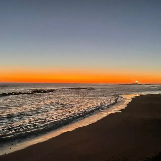 El sol se está poniendo sobre el océano y una persona está caminando por la playa.