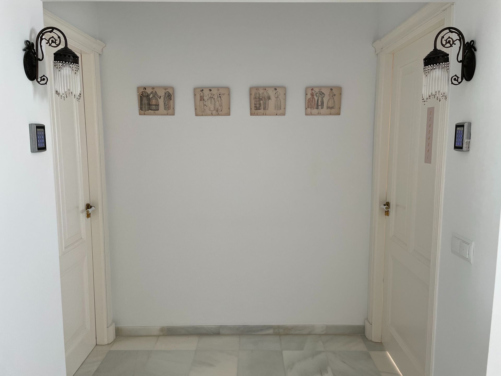 Un pasillo con puertas blancas y algunos cuadros en la pared.