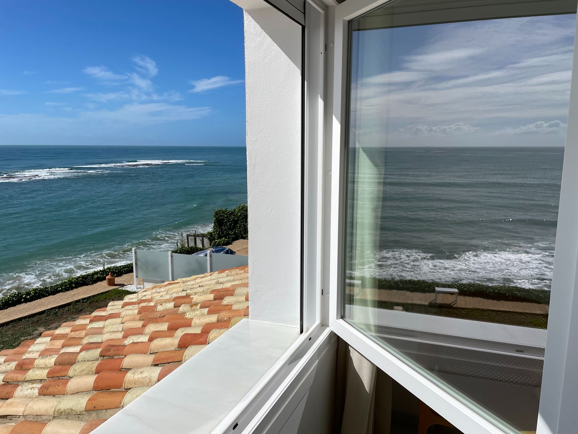 Una vista del océano desde una ventana con techo de tejas.
