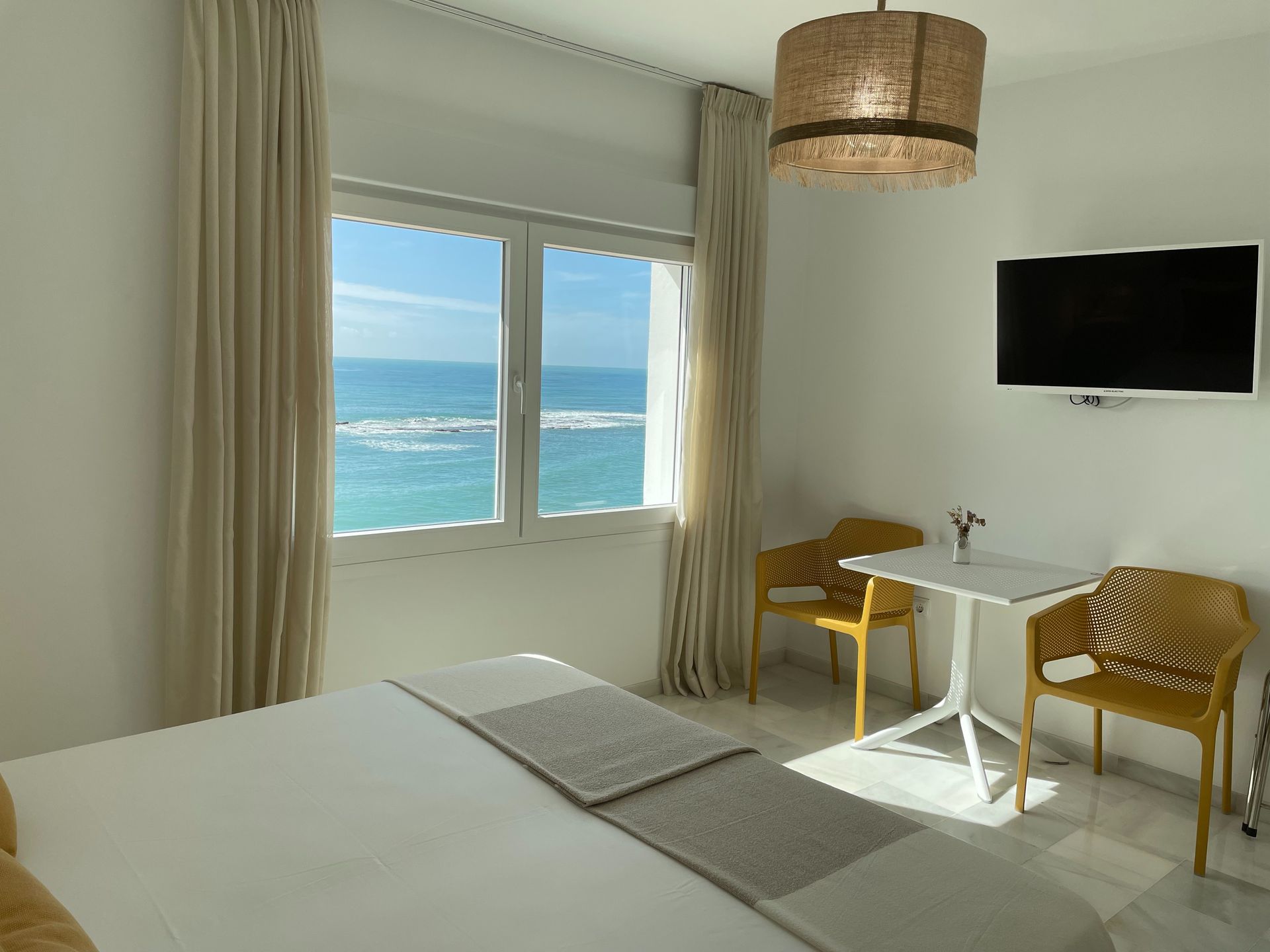 Una habitación de hotel con cama, sillas, mesa y televisión con vista al océano.
