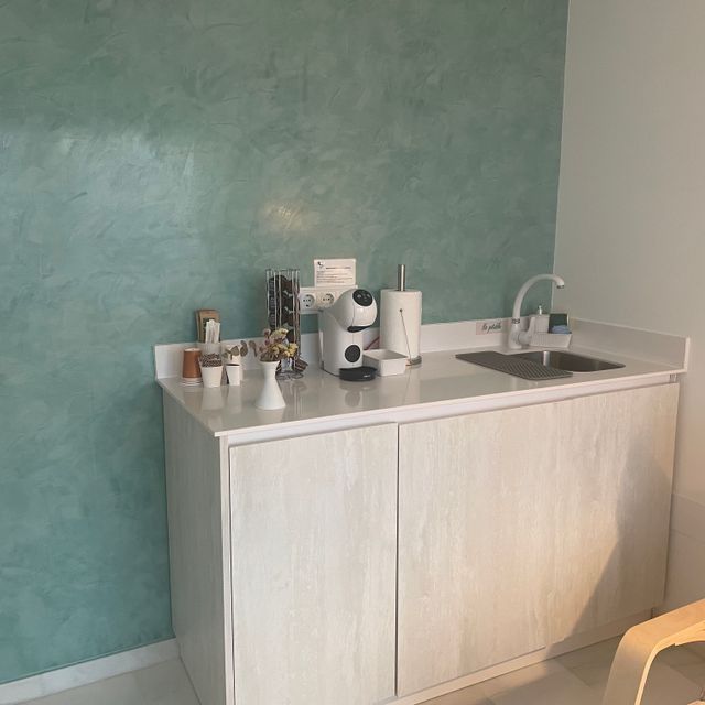 Una cocina con gabinetes blancos y una pared verde.