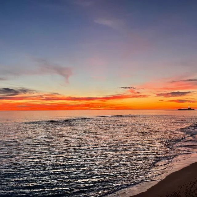 Una puesta de sol sobre el océano con una playa en primer plano.