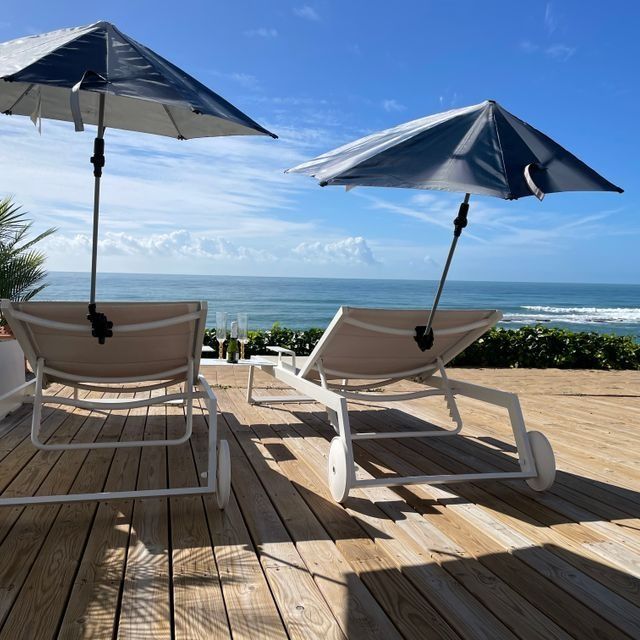 Dos tumbonas con sombrillas en una terraza con vista al océano.