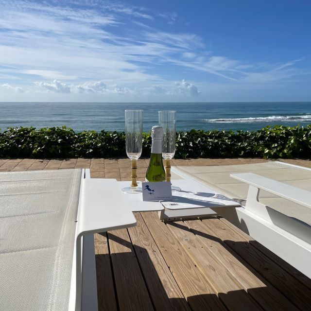 Dos copas y una botella de champán en una mesa con vistas al océano.
