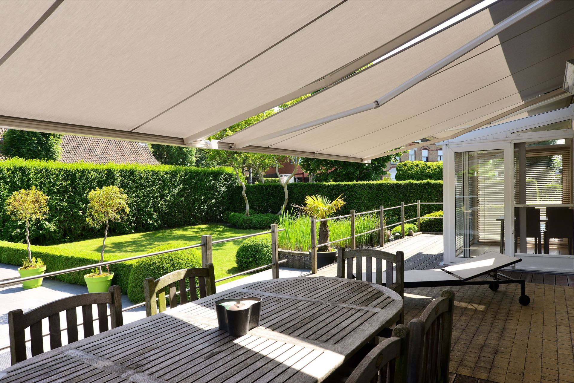 Grande table sur une terrasse en bois sous deux stores bannes