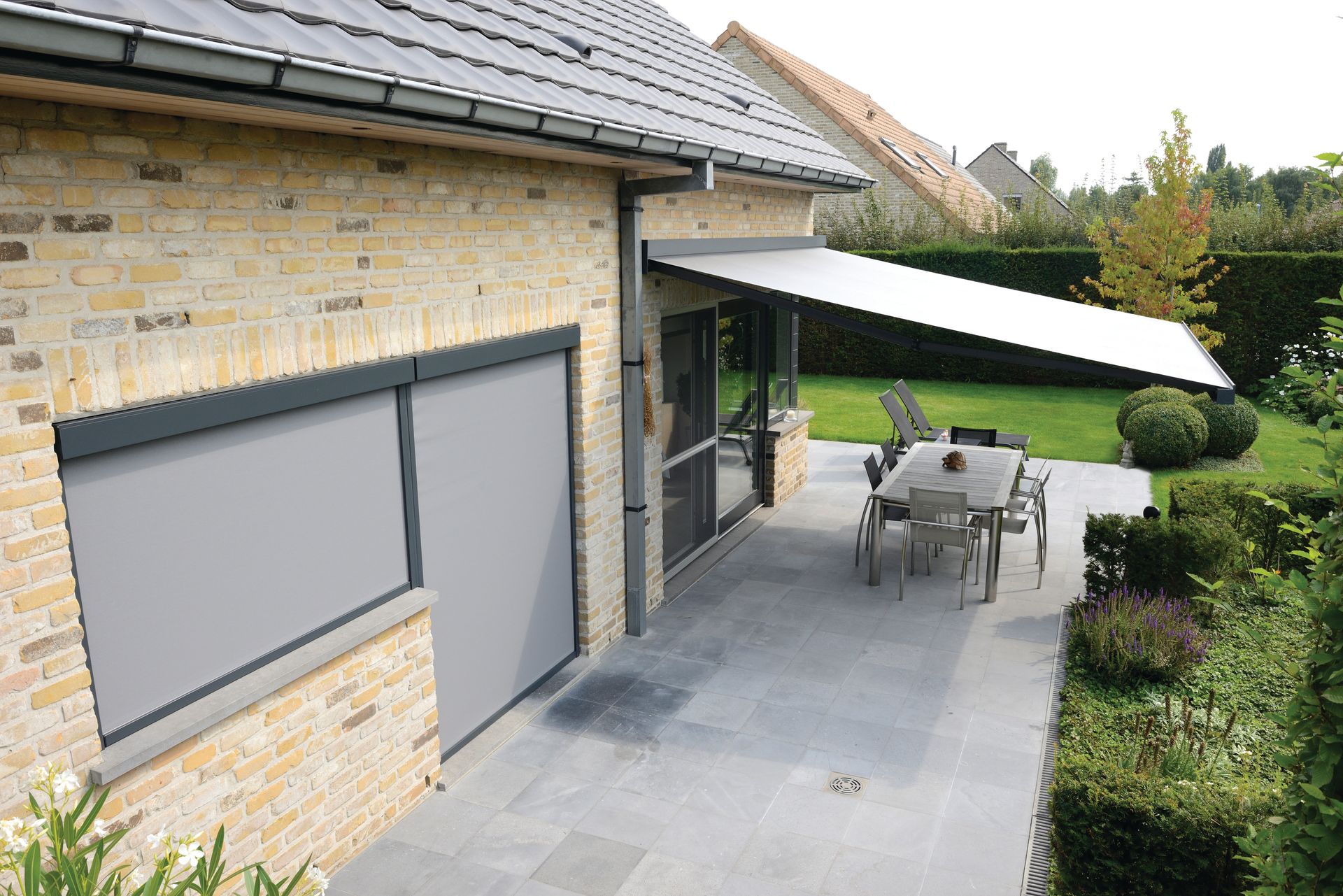 Vue légèrement du dessus d'une maison avec stores extérieurs aux fenêtres fermés et store banne ouvert