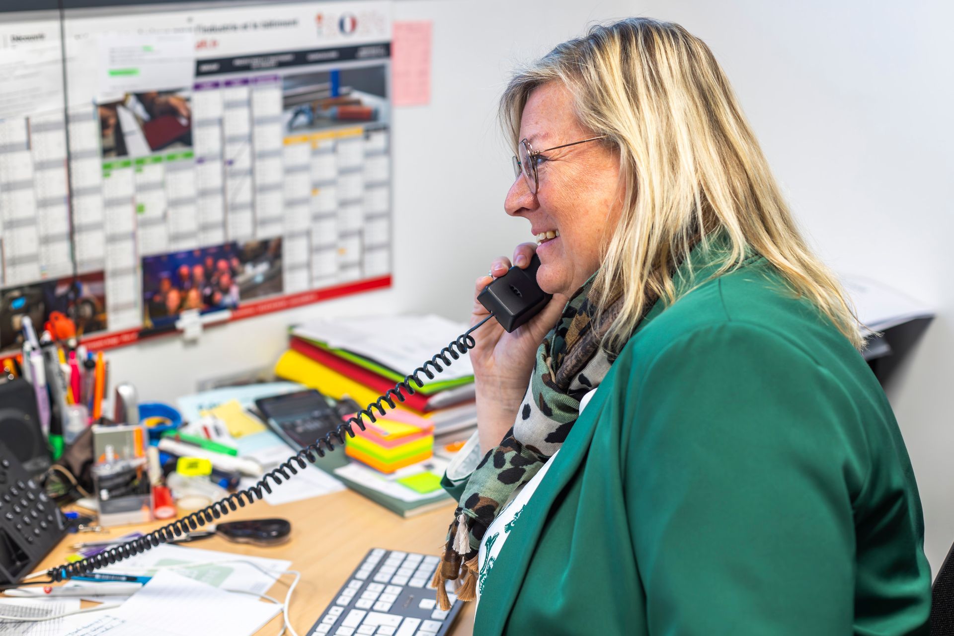 Une dame souriante à la veste verte au téléphone à son bureau
