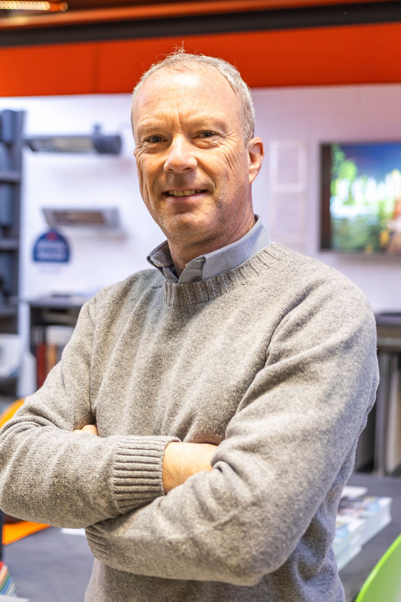 Un homme souriant portant un pull gris, croisant les bras