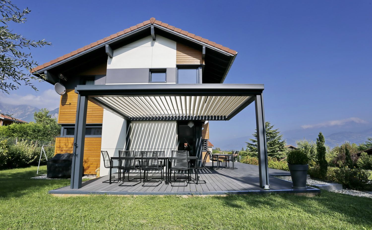 Pergola au-dessus d'une terrasse devant une maison sur deux niveaux