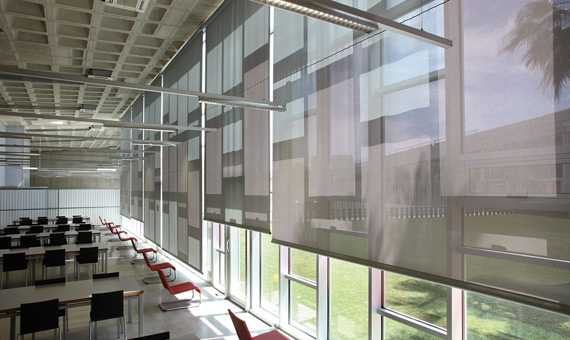 Plusieurs stores en tissu presque tous fermés le long des baies vitrées d'un open space