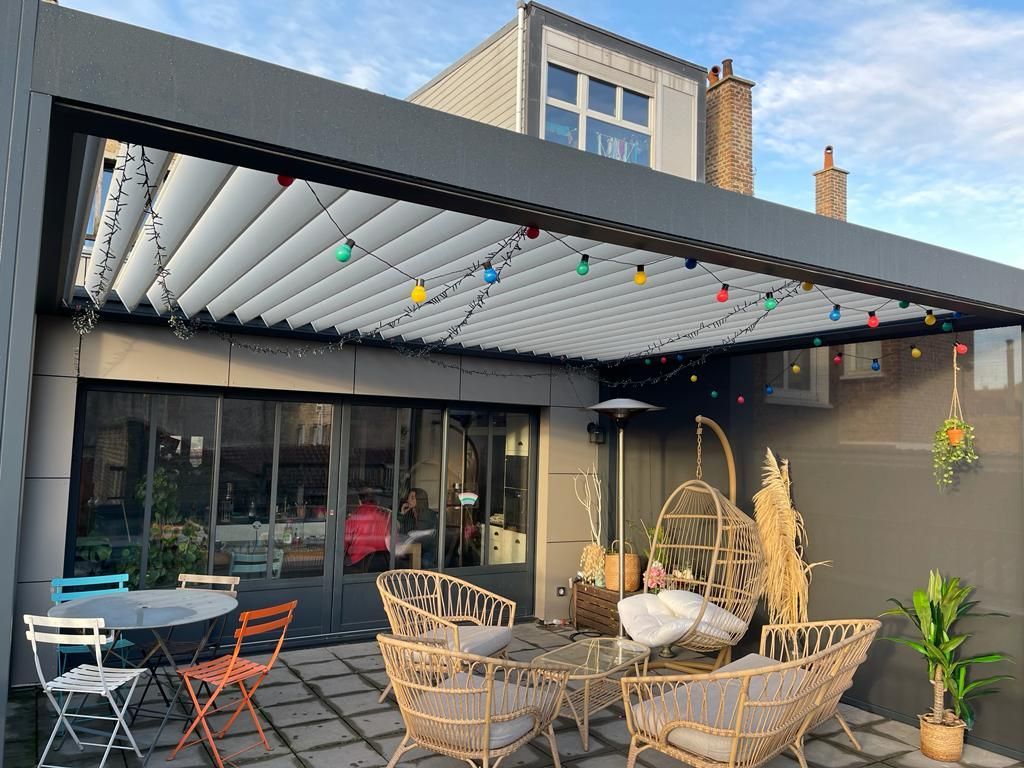 Terrasse d'un appartement avec plusieurs tables et chaises sous une pergola décorée de guirlandes
