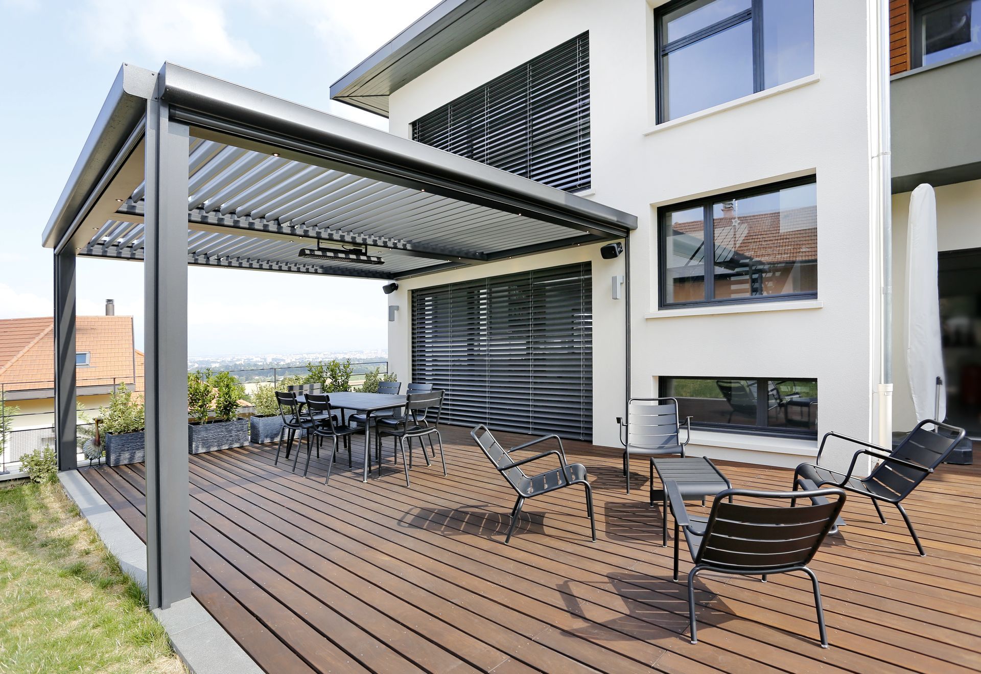 Terrasse en bois avec sièges et tables sous une pergola bioclimatique