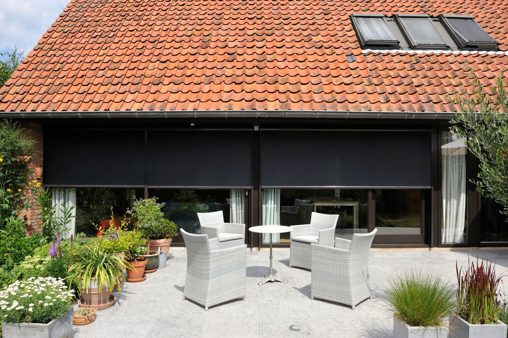 Deux stores extérieurs à moitié fermés devant une terrasse avec quatre sièges en osier