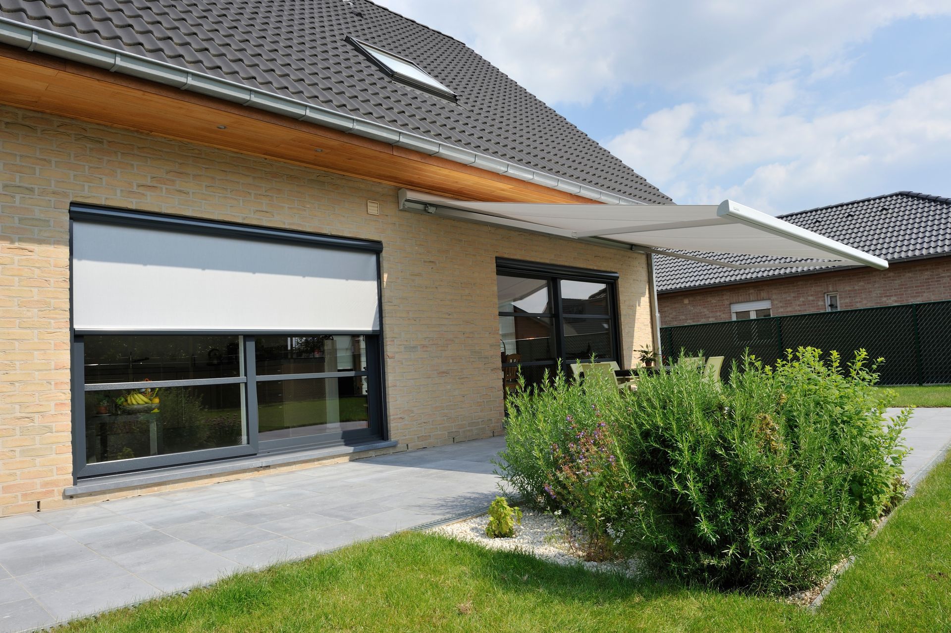 Façade d'une maison avec un store banne et un store extérieur à moitié ouvert