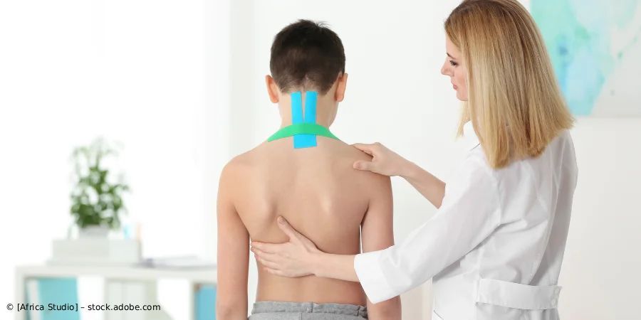 Ein Arzt untersucht den Rücken eines Patienten, der Kinesiologie-Tape im Nackenbereich trägt.