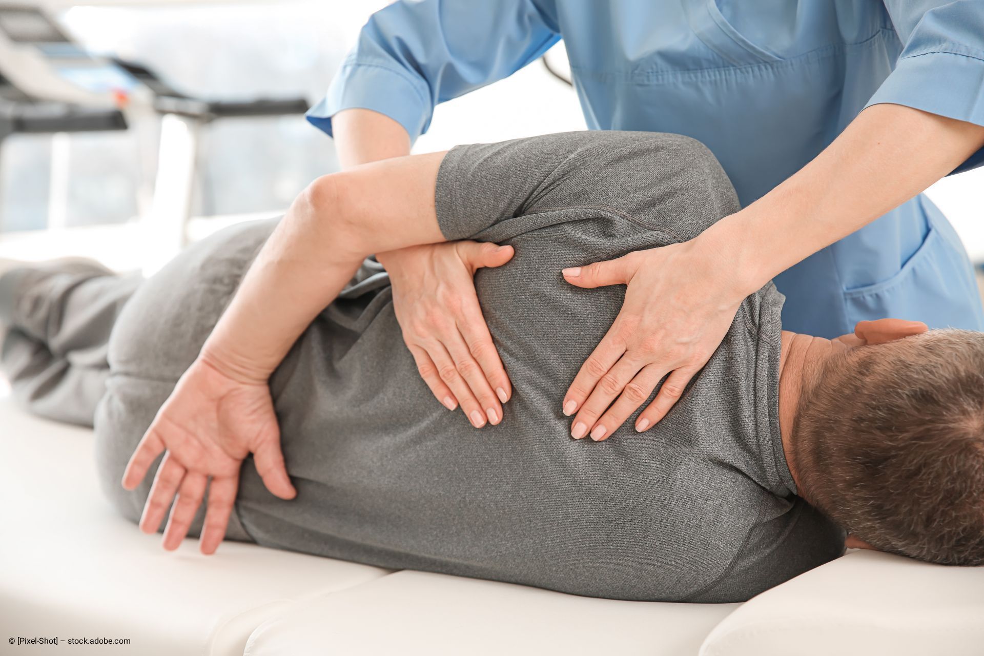 Eine Person, die sich auf einer weißen Liege einer Physiotherapie unterzieht, wobei ein Therapeut ihren Rücken justiert.