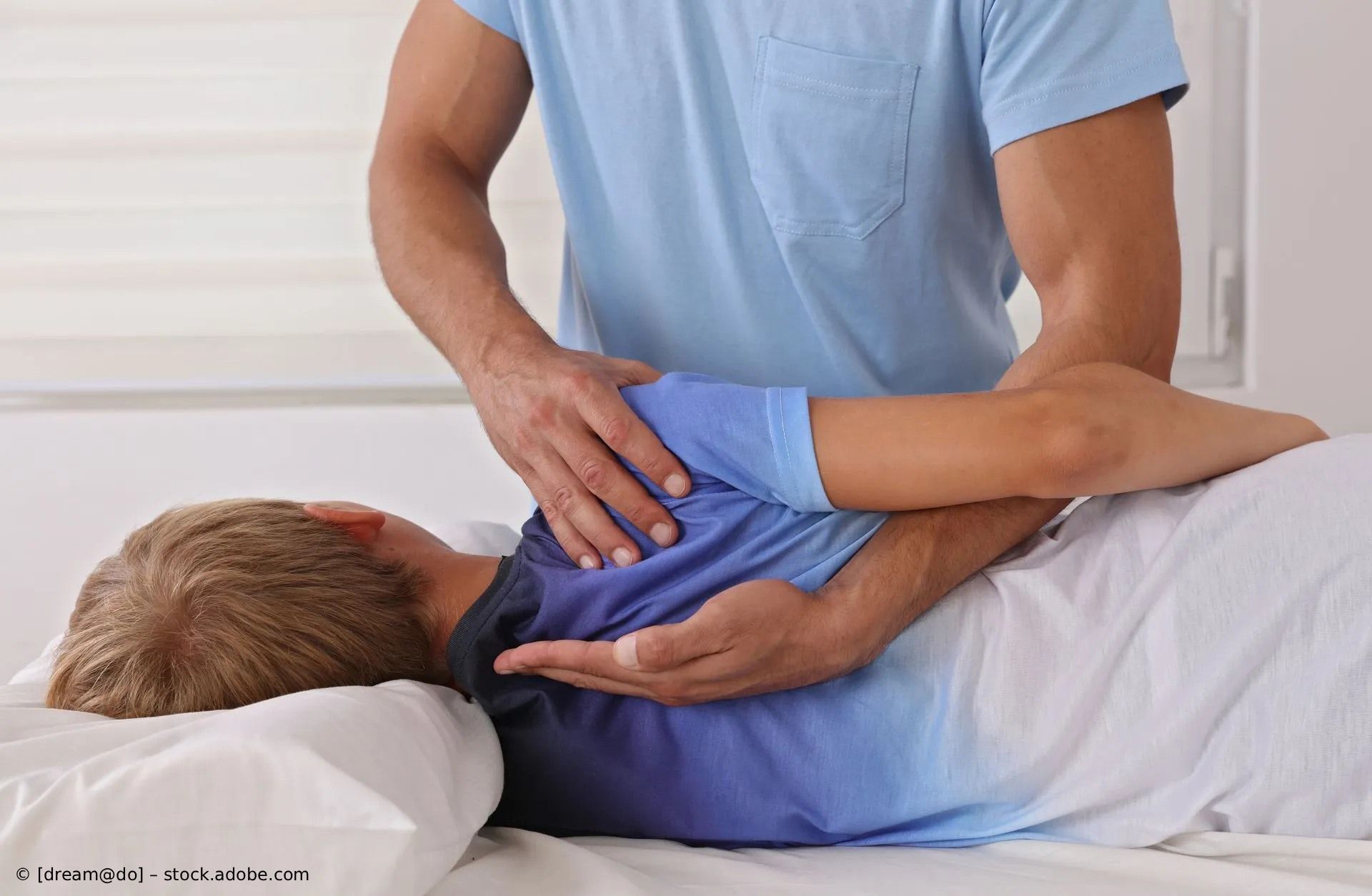 Eine Person erhält eine Schulterkorrektur auf einer Massageliege; der Therapeut manipuliert mit den Händen den Arm 