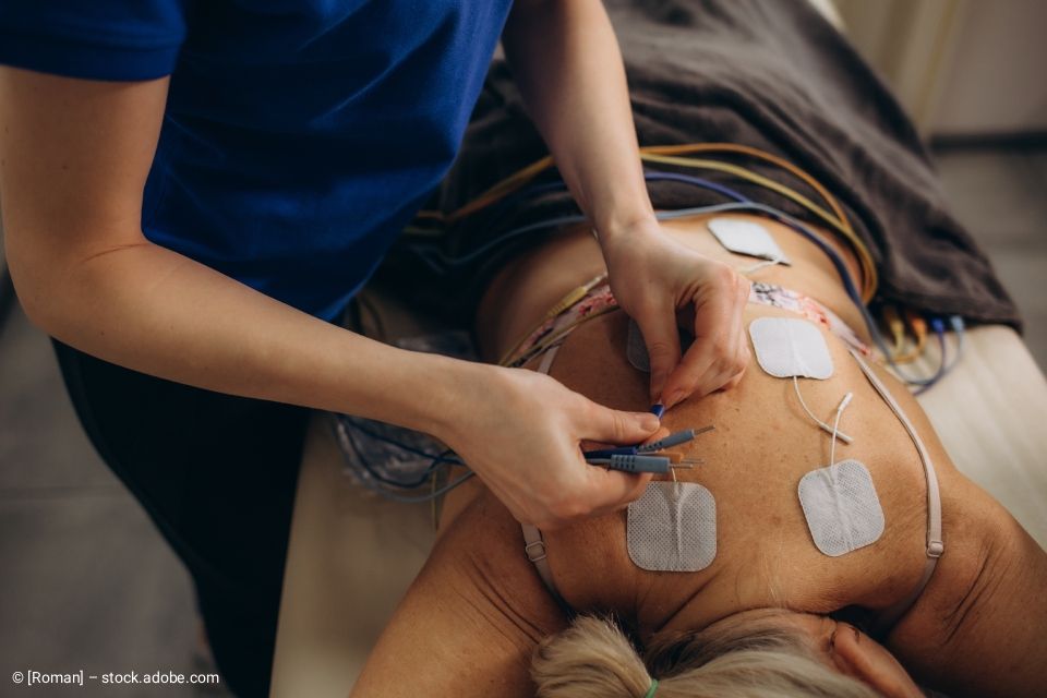 Während eines medizinischen Eingriffs befestigt ein Therapeut Elektroden am Rücken des Patienten.