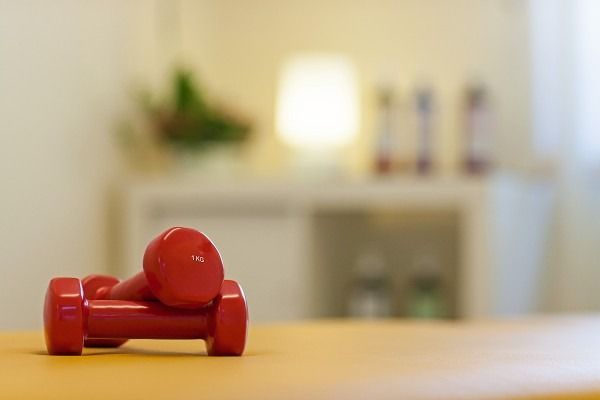 Rote Hanteln auf gelbem Grund, im Hintergrund ist ein verschwommenes Wohninterieur zu sehen.