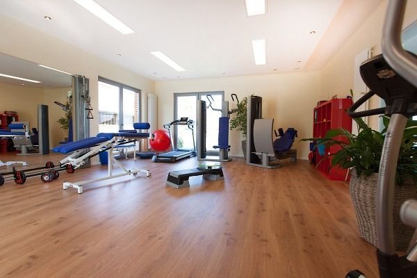 Fitnessstudio-Interieur mit Trainingsgeräten auf Holzboden. Sonnenlicht strömt durch die Fenster.