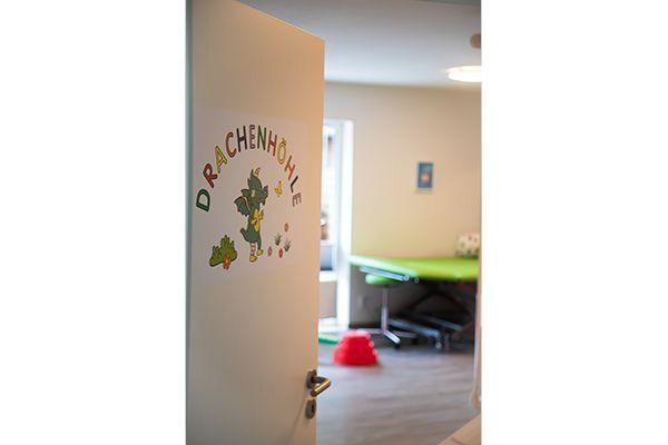 Ein Türbogen mit dem Logo „Drachenhöhle“ (Dragon's Den) führt in einen Raum mit einem grünen Tisch.